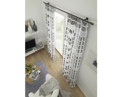 Woonkamer met gordijnen met patroon, gordijnroede, fauteuil, vloerkleed en salontafel.