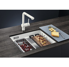 Spoelbak met kraan, snijplank en etenswaren op een aanrecht.