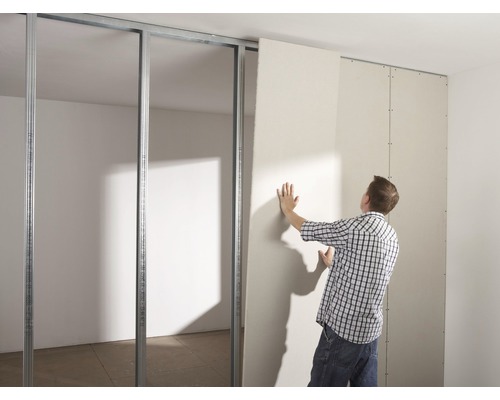 Een man monteert een gipsplaat op een metalen frame binnenshuis.