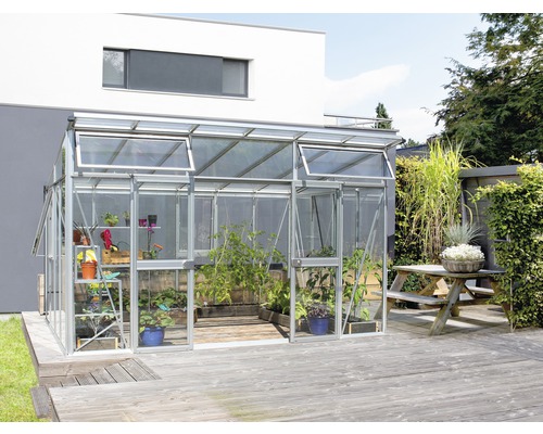 Kas met planten op houten terras voor een woonhuis.
