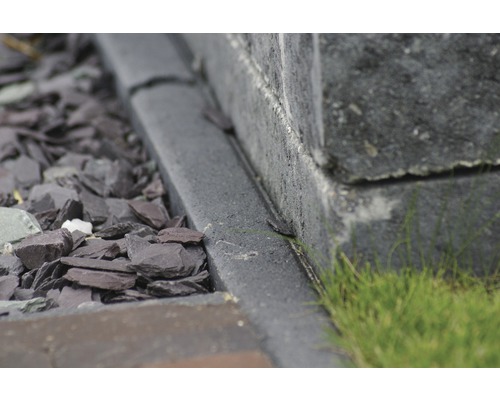 Close-up van een stenen muur met een trottoirband en decoratief grind in de tuin.