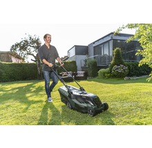 Een man maait het gras met een grasmaaier in de tuin.