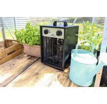 Kas met elektrische kachel, planten en gieter op houten tafel