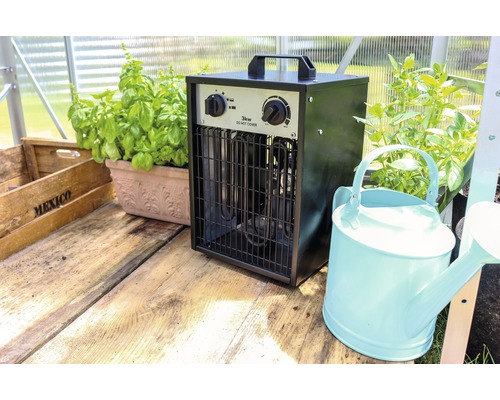 Kas met elektrische kachel, planten en gieter op houten tafel
