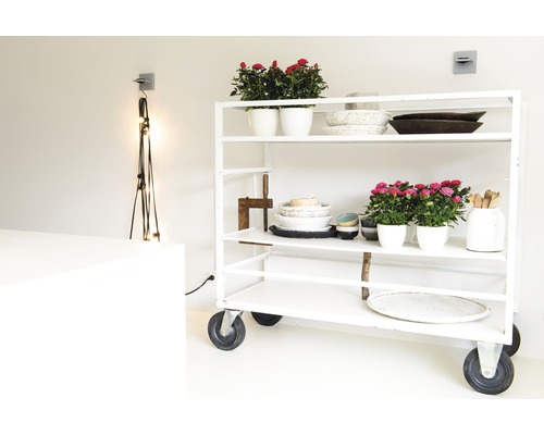 Een witte rolwagen met bloempotten, schalen en decoratieve objecten in een heldere ruimte.