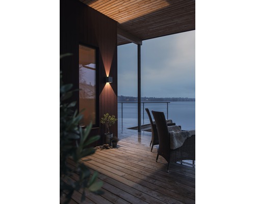 Scene van een houten terras met een buitenmuurlamp, stoelen en uitzicht op een meer