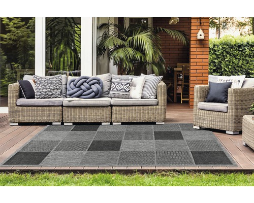 Buitenscène met een grijs geblokt tapijt en rotan zitmeubelen op een terras