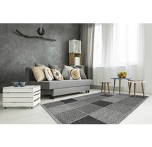 Woonkamer met grijze bank, salontafel van houten kisten en vloerkleed met vierkant patroon