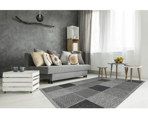 Woonkamer met grijze bank, salontafel van houten kisten en vloerkleed met vierkant patroon