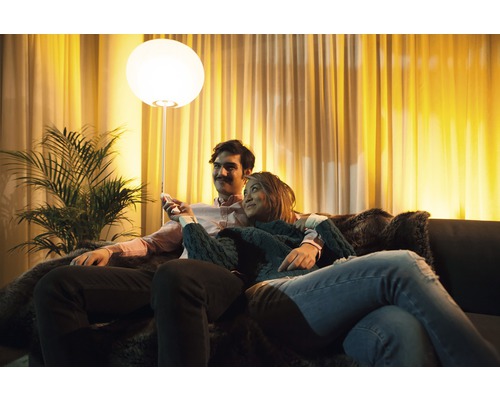 Stel zit op een bank in een lichte woonkamer met een vloerlamp en kamerplant.