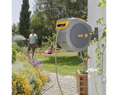 Tuinscène met gemonteerde slangenbox, gezin op de achtergrond en man die de tuin besproeit.
