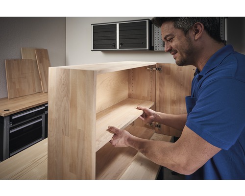 Een man monteert een houten kast met planken in een werkplaats.