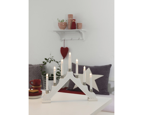 Witte houten adventskandelaar met zeven LED-kaarsen op een tafel met decoraties
