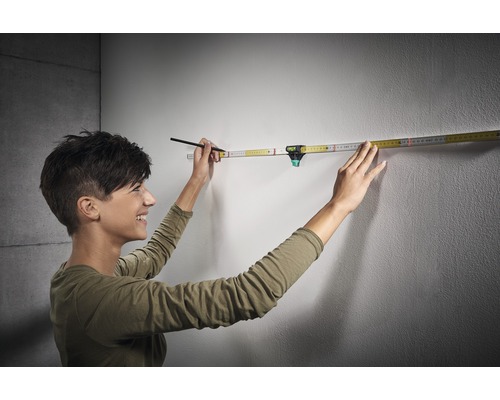 Vrouw gebruikt een duimstok met geïntegreerde waterpas op een muur