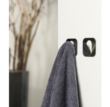 Twee metalen handdoekhaken aan een witte muur, één met een grijze handdoek
