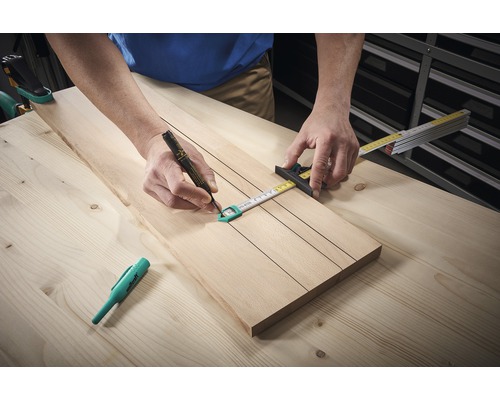 Een persoon tekent met een stift lijnen op een houten plank met een duimstok.