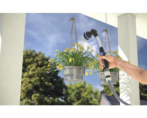 Een persoon bewaterd hangende bloembakken met een tuinspuit.