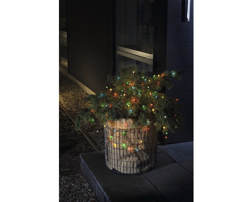 Decoratieve kerstboom met lampjes in een jute zak en draadmand buitenshuis.