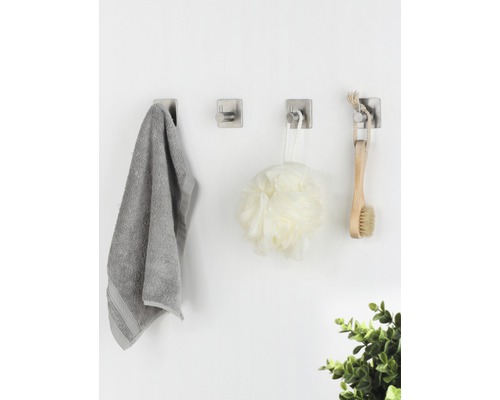 Drie wandhaken met handdoek, douchebal en borstel aan een muur