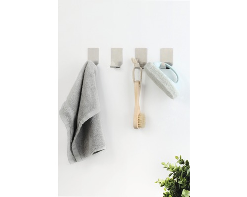 Vier wandhaken met handdoek, borstel en badspons aan een wand