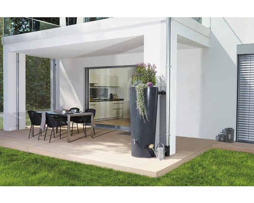 Buitenscène met een regenton naast een regenpijp, een gieter en een eettafel op een terras