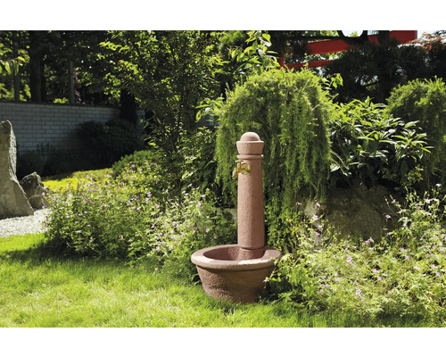 Tuin fontein van steen met kraan in een groene tuinomgeving.