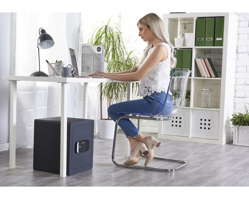 Een vrouw werkt aan een bureau met een bureaulamp, een laptop en een kluis in een kantoorruimte.