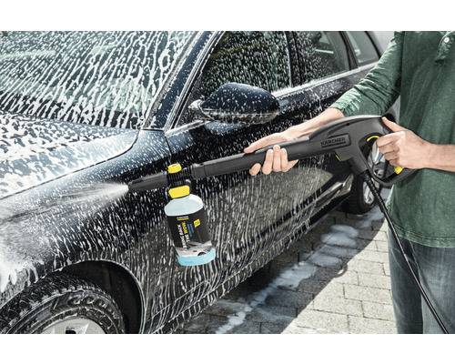 Een persoon reinigt een auto met een Kärcher hogedrukreiniger en reinigingsmiddel.