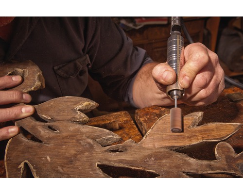 Ambachtsman bewerkt houten snijwerk met roterend gereedschap.