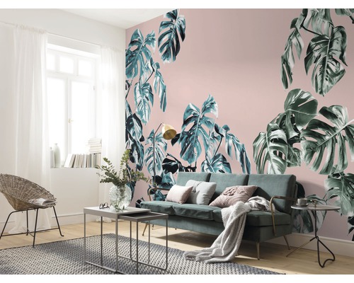 Woonkamer met Monstera-behang, bank en rotan stoel.
