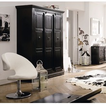 Interieurscène met een zwarte kledingkast, een witte stoel en decoratieve lantaarns in een lichte kamer.