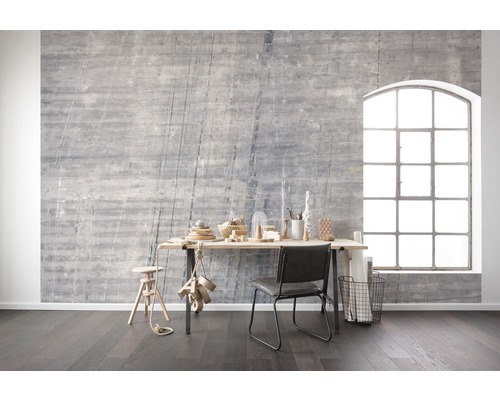 Woonkamer met grijze betonnen muur, bureau, stoel en groot raam voor een lichte en moderne sfeer.