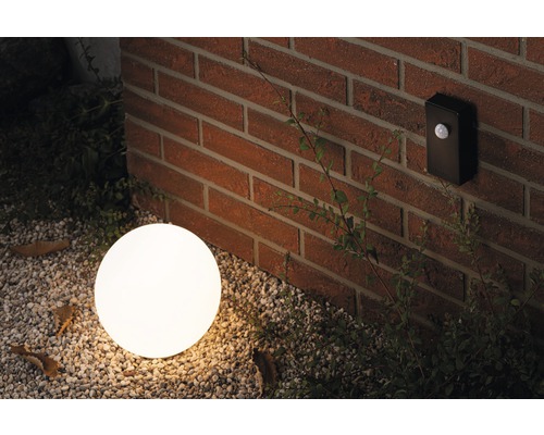 Scene met een ronde buitenlamp en een bewegingsmelder aan een bakstenen muur