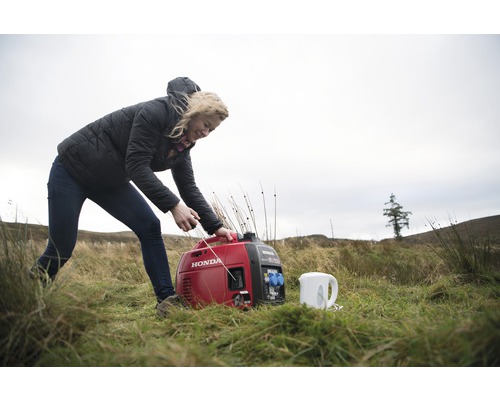 Een vrouw start een rode Honda generator buiten naast een waterkoker