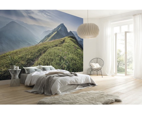 Lichte slaapkamer met fotobehang van een berglandschap, bed, stoel, lamp en een lichte houten vloer