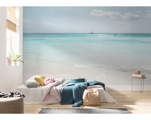 Woonkamer met fotobehang dat een zeegezicht met strand en een zeilboot toont.