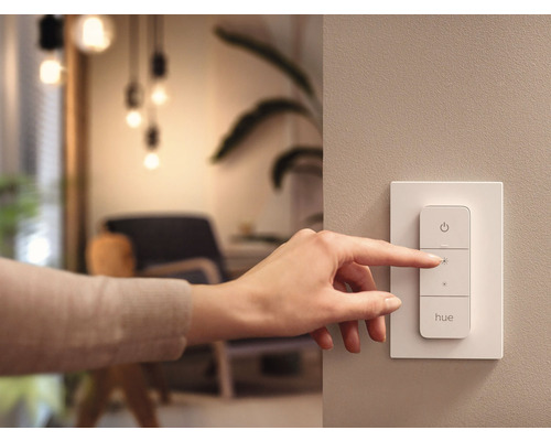 Een hand bedient een Philips Hue dimschakelaar aan de muur.