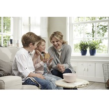 Een moeder en haar kinderen zitten op een bank en eten koekjes in een lichte woonkamer.