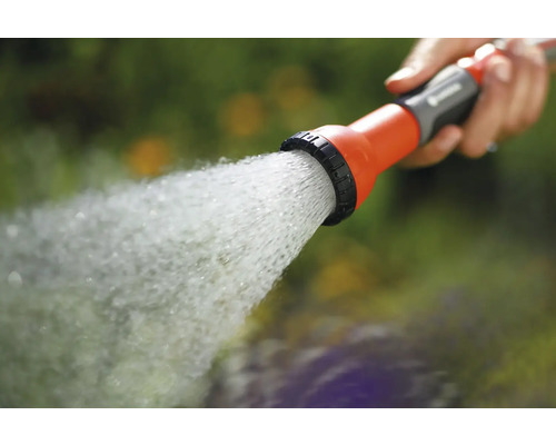 Een hand houdt een tuinspuit vast waar water uit komt.