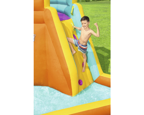 Jongen klimt op een opblaasbare waterglijbaan in de tuin