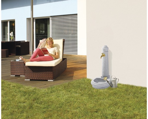 Tuinscene met ligstoel, fontein en lezende vrouw