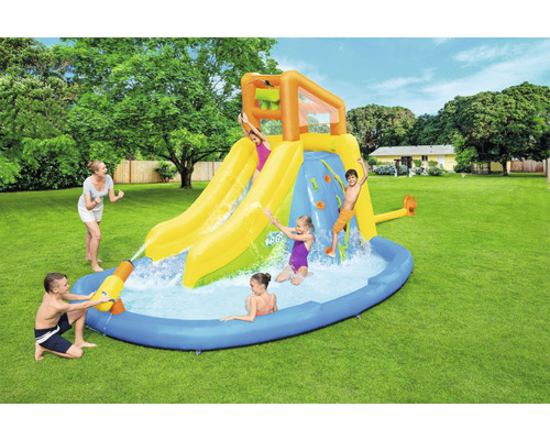 Opblaasbaar waterpark met glijbanen, klimwand en zwembad in de tuin met spelende kinderen.