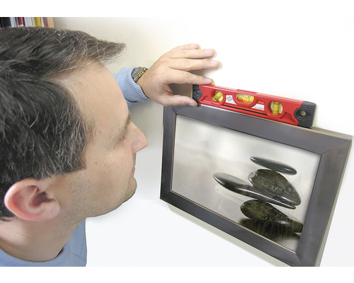 Een persoon richt een ingelijste foto waterpas met een waterpas.