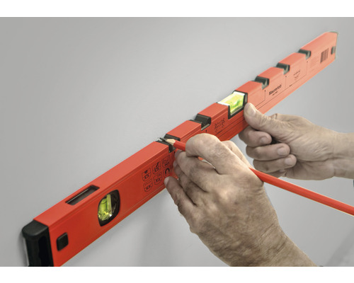 Een waterpas wordt met een potlood op een muur uitgelijnd.