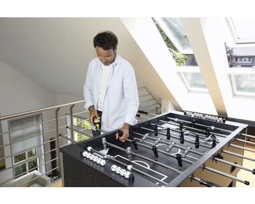 Man meet een tafelvoetbaltafel in een lichte kamer met dakramen