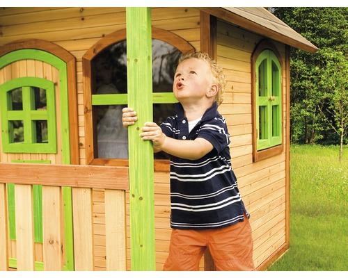 Jongen speelt voor een houten speelhuis met ramen