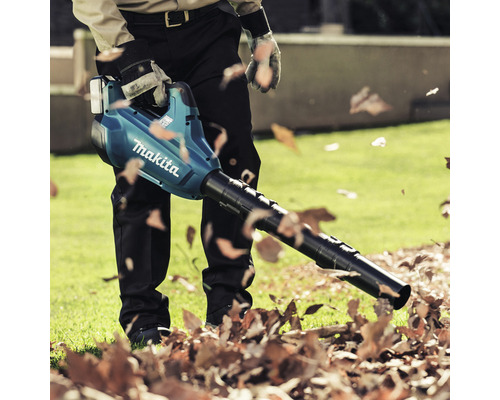 Een man gebruikt een Makita bladblazer in de tuin om bladeren te verwijderen.