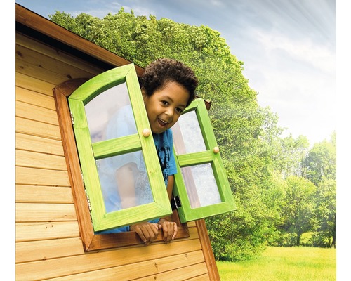 Jongen kijkt uit het raam van een houten speelhuis