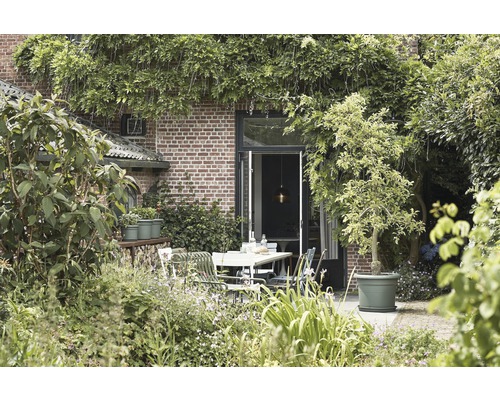 Tuinscene met eettafel, stoelen, planten en een bakstenen gebouw op de achtergrond