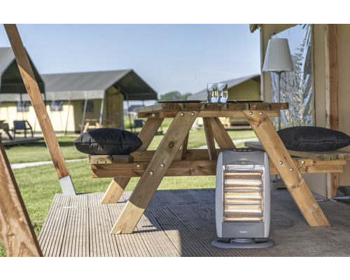 Scene met een houten picknicktafel, kussens en een verwarming voor tenten